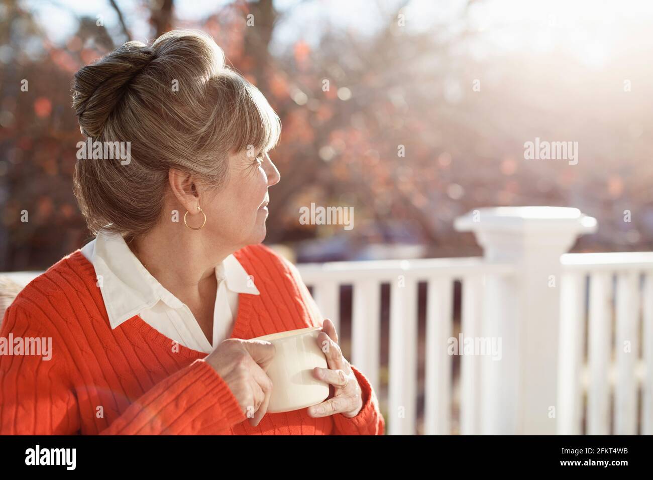Senior woman drinking coffee and looking over shoulder from porch Stock Photo