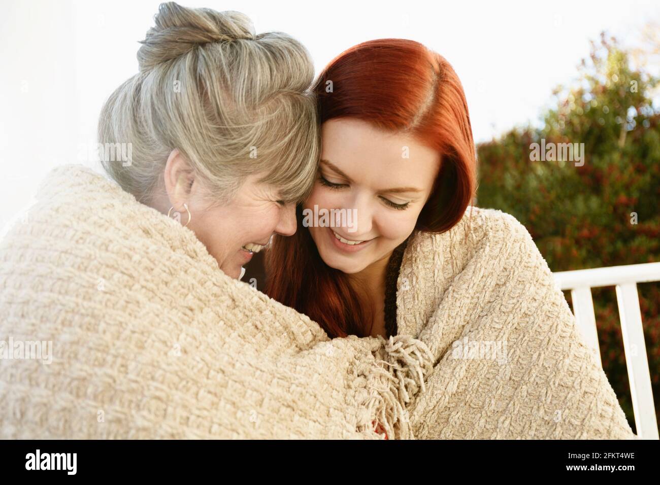 Senior woman and adult daughter face to face wrapped in a blanket on porch Stock Photo