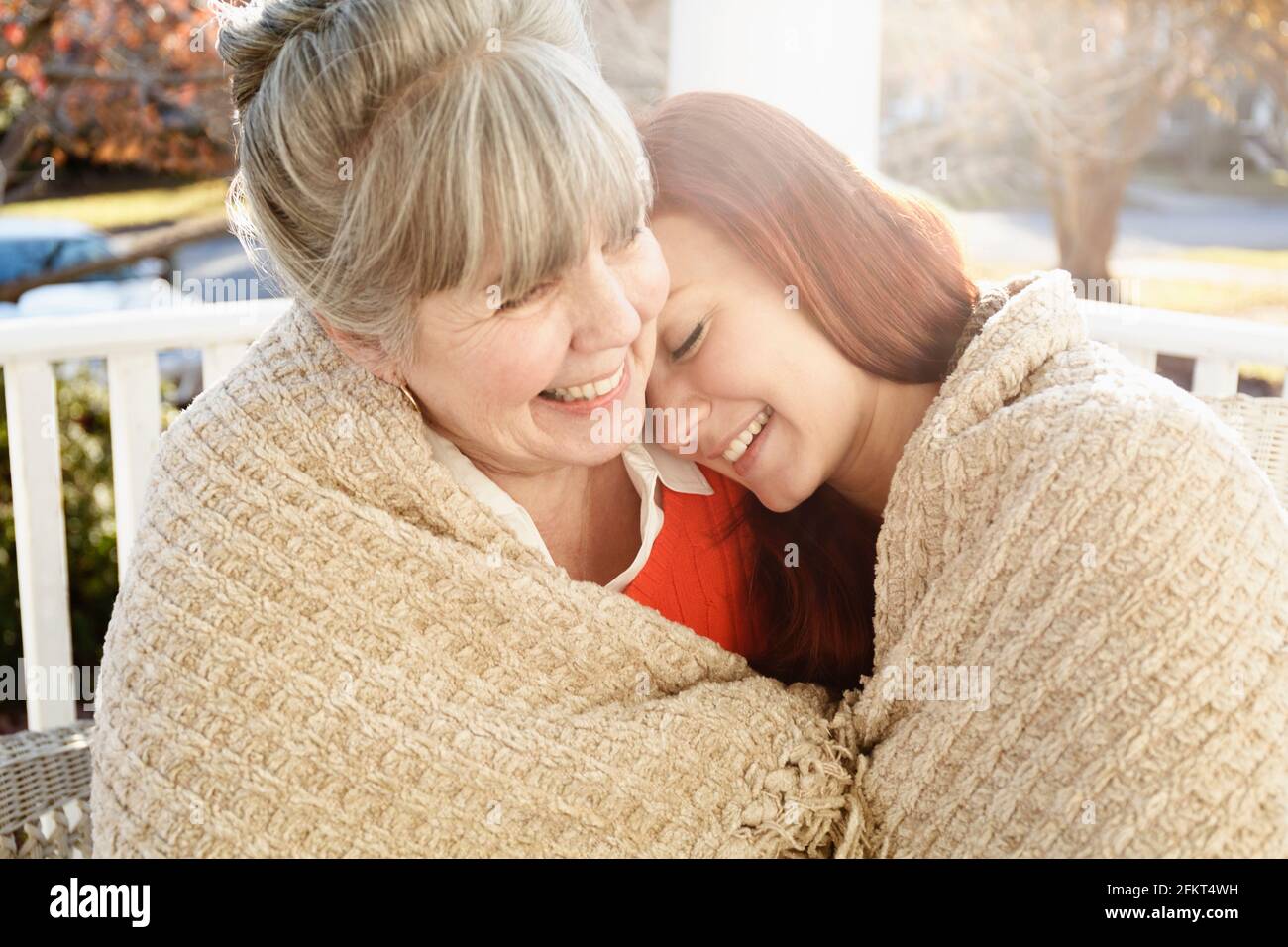 Senior woman and adult daughter wrapped in a blanket on porch Stock Photo