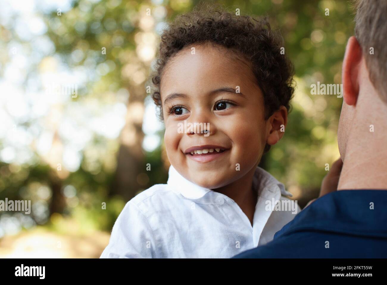 Over shoulder view of father carrying preschool boy looking away smiling Stock Photo