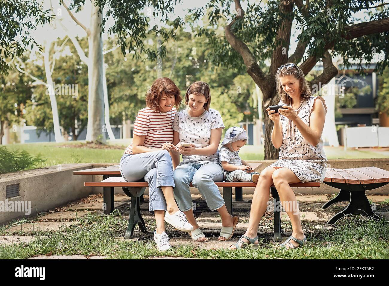 Three women friends with baby strollers reading text message in park Stock Photo