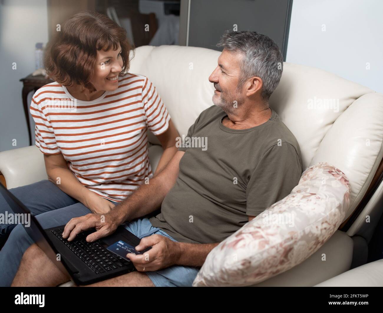 Smiling middle aged couple sitting on their couch using the laptop to buy online at home Stock Photo