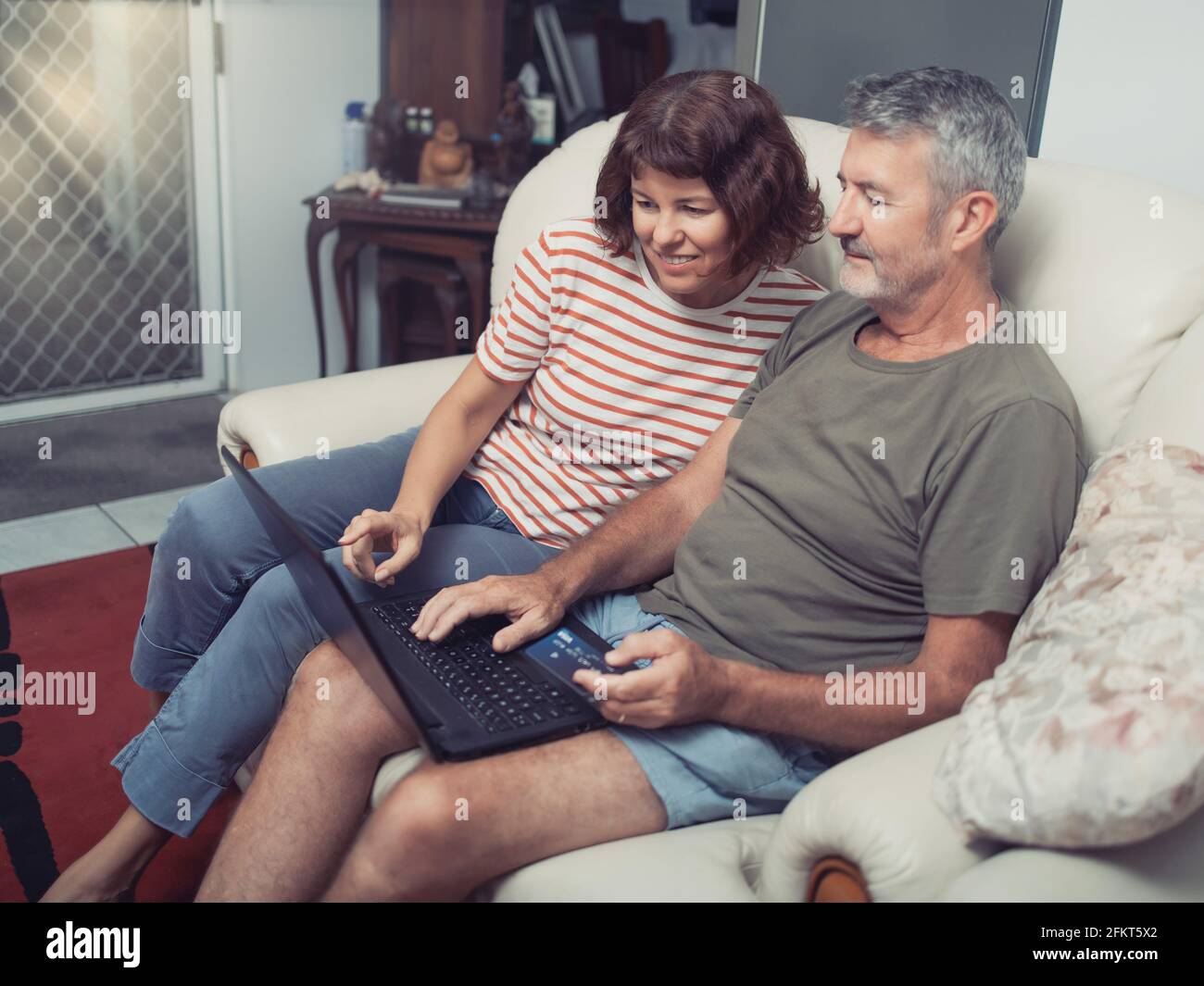 Smiling middle aged couple sitting on their couch using the laptop to buy online at home Stock Photo