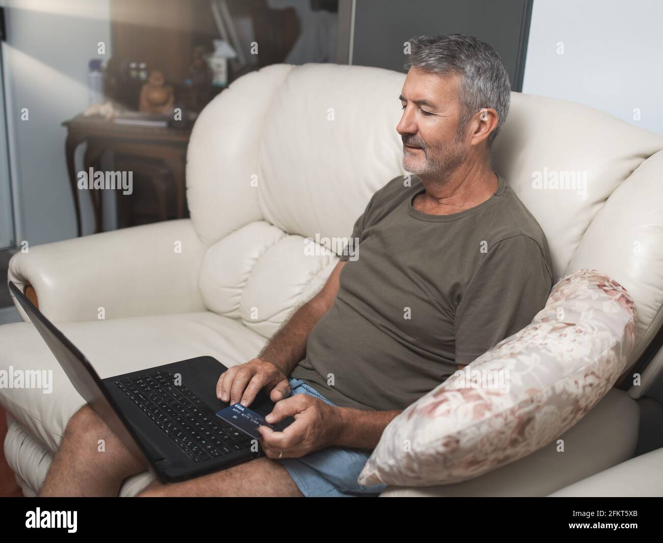 Smiling middle aged man sitting on the couch using the laptop to buy online at home Stock Photo