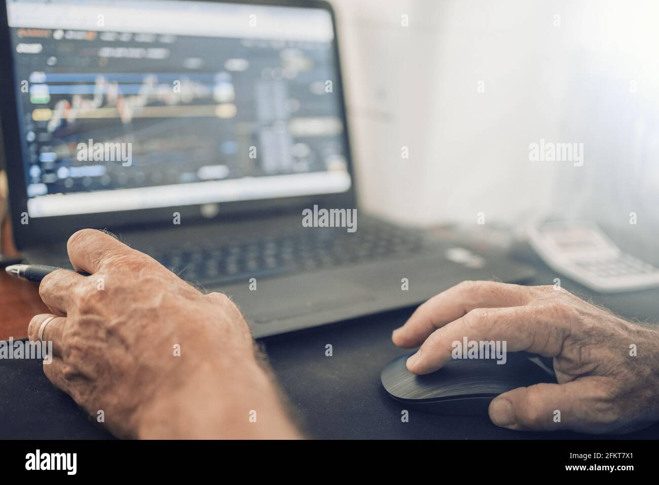 A senior man sitting at a desk in front of a laptop computer Stock Photo
