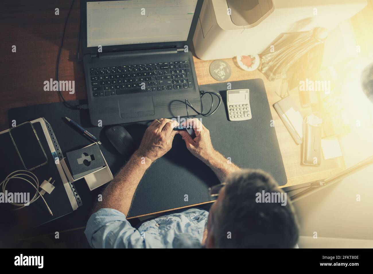 A senior man sitting at a desk in front of a laptop computer Stock Photo
