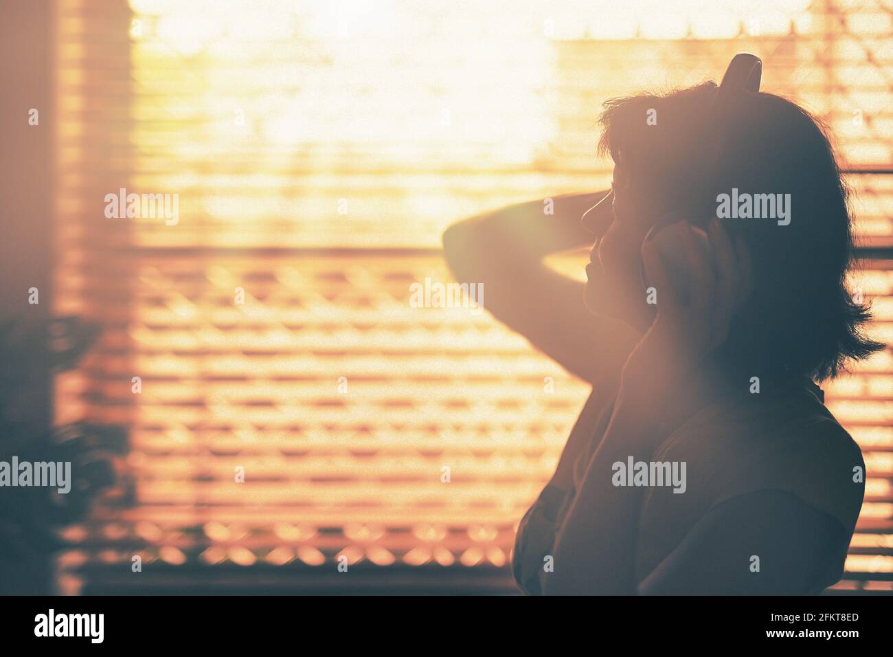 A silhouette of woman with Headphone or Headset on her head with the window and sunlight on background. Stock Photo