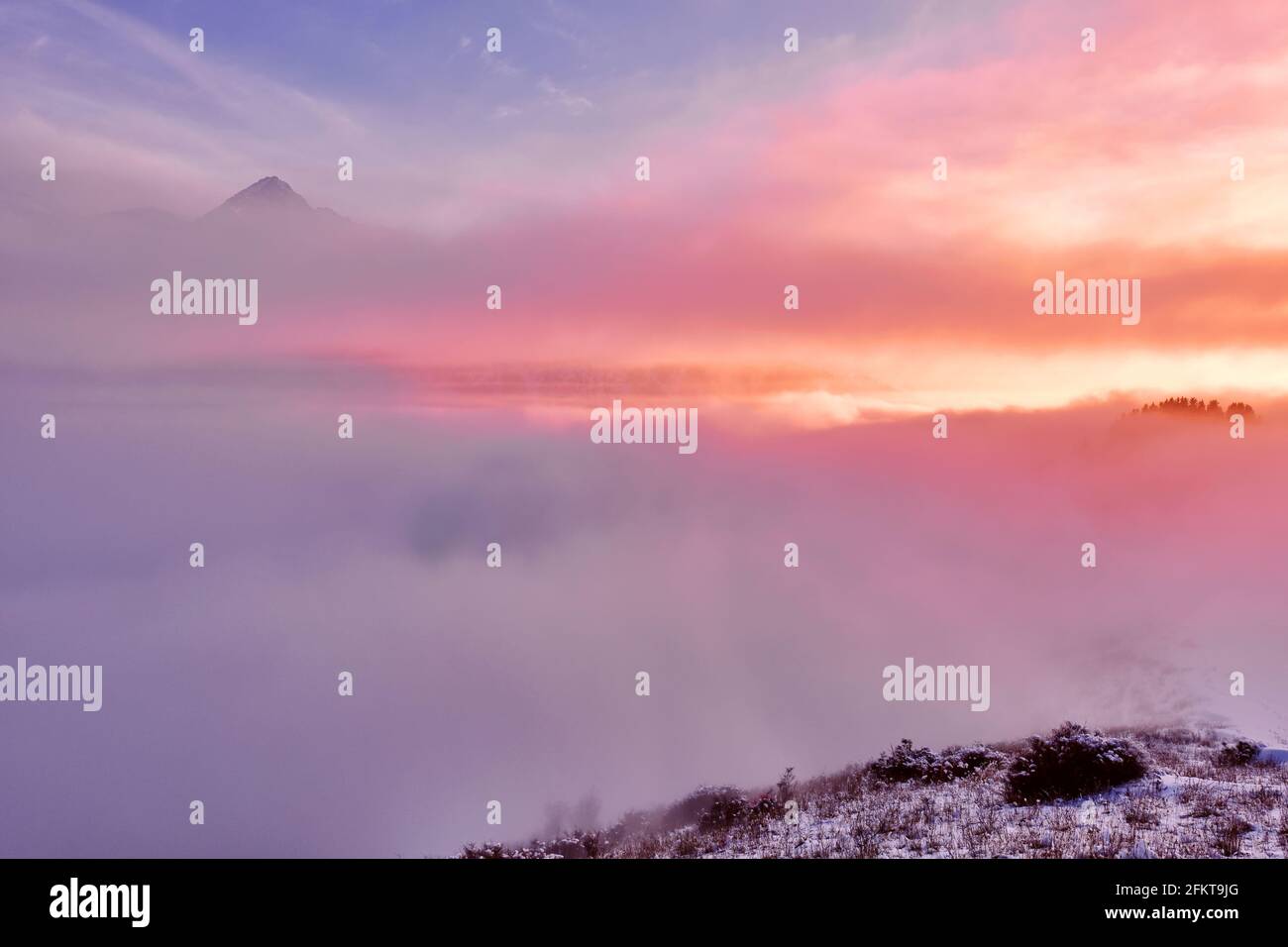 Fairy cloudy atmosphere in the mountains at sunset; rocky and forest peaks hid behind a wall of clouds Stock Photo