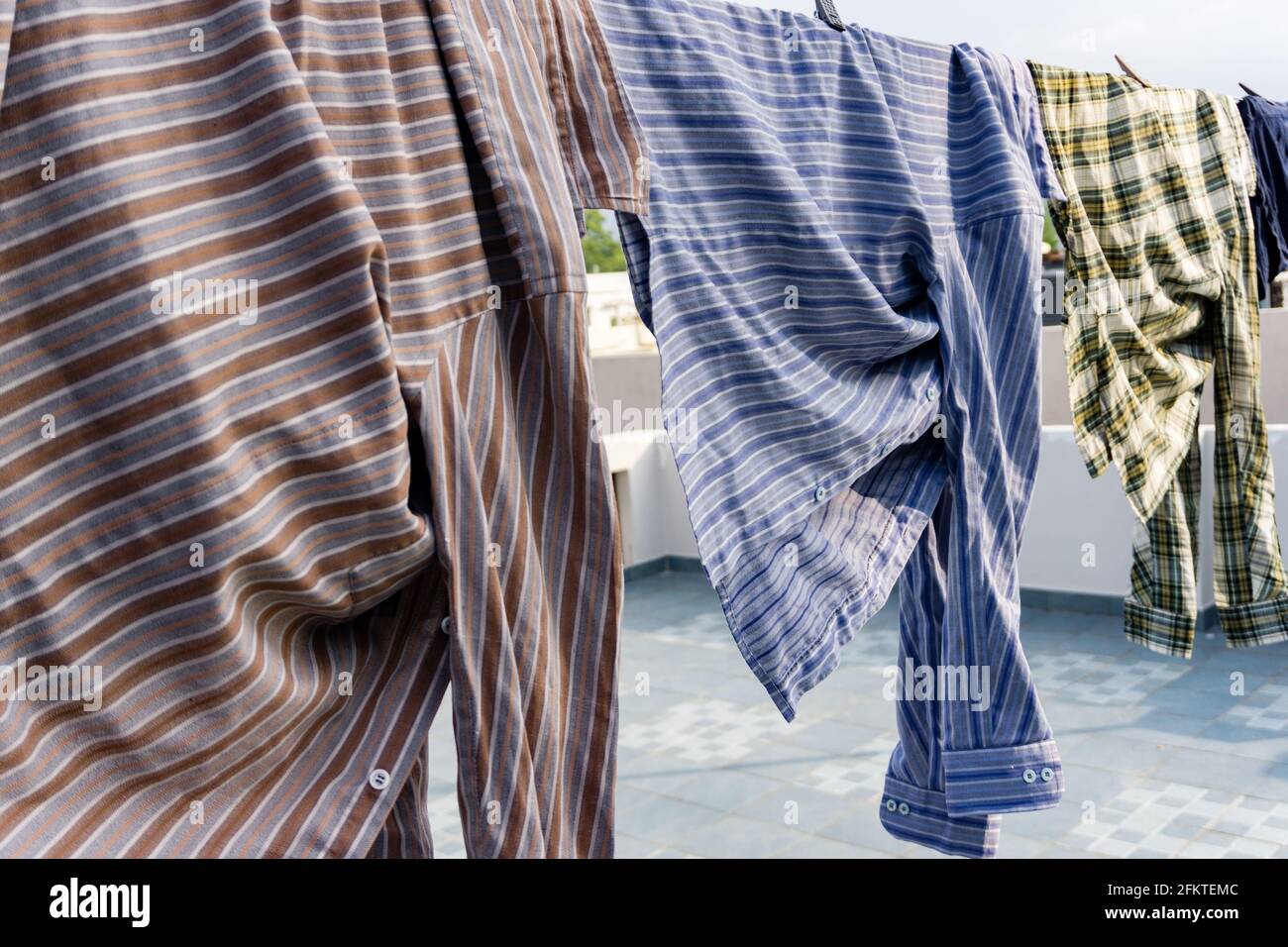 https://c8.alamy.com/comp/2FKTEMC/a-close-up-shot-of-laundry-drying-outside-under-sun-shirts-hanging-on-a-wire-at-roof-2FKTEMC.jpg
