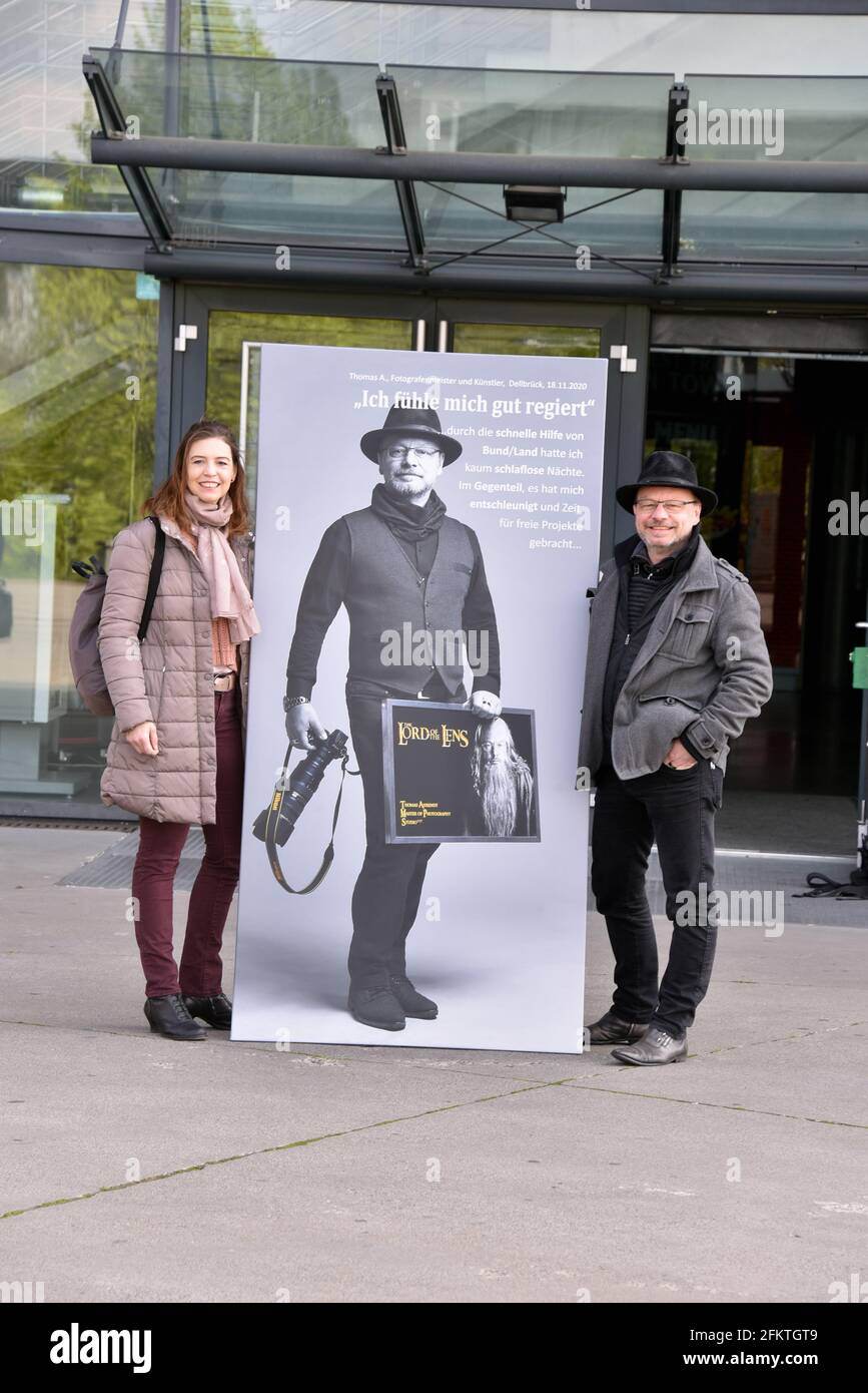 03 May 2021, North Rhine-Westphalia, Cologne: Artist and photographer Thomas Ahrendt and his wife pose at his opening of the exhibition "Der Stadt Bestes - Das Gute in der Krise". The 70 large-format pictures can now be seen at ground level on the windows of the Lanxess Arena Photo: Horst Galuschka/dpa Stock Photo
