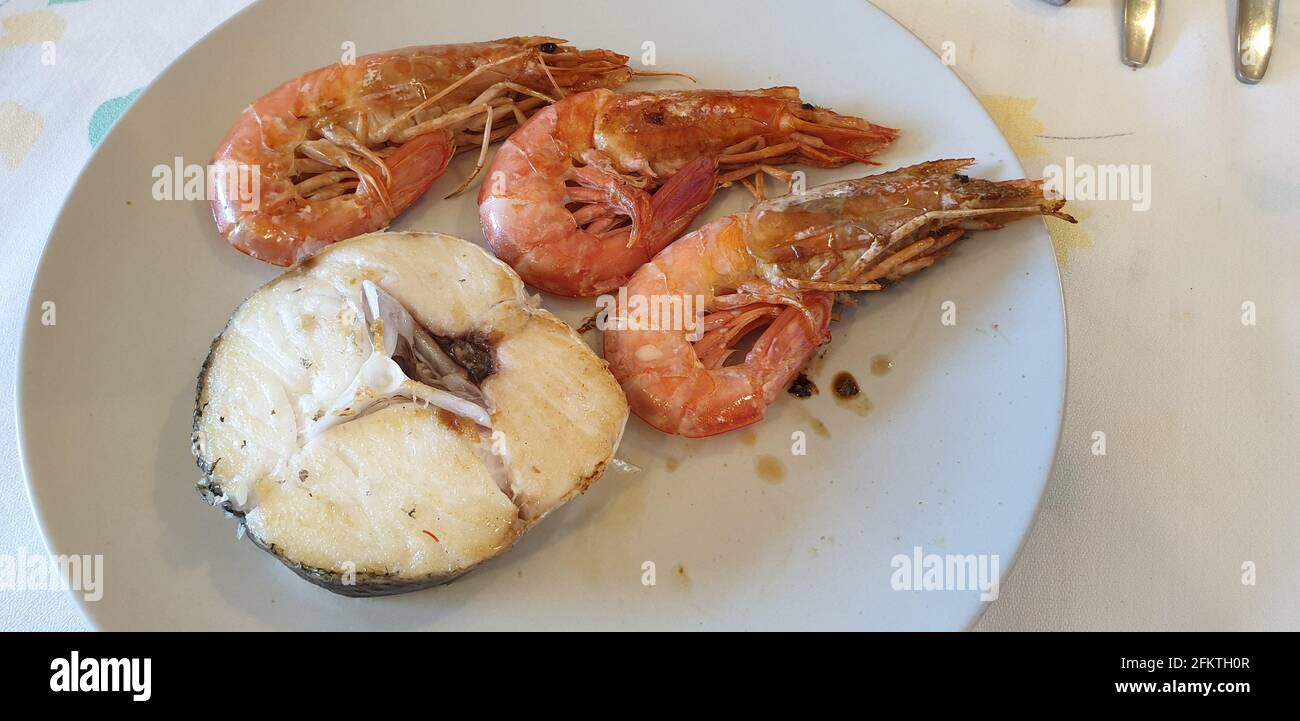 Grilled hake with prawns. It is an easy, simple, fast, and ideal recipe for when we don´t know how to cook. Heat a drizzle of oil on the grill and Stock Photo