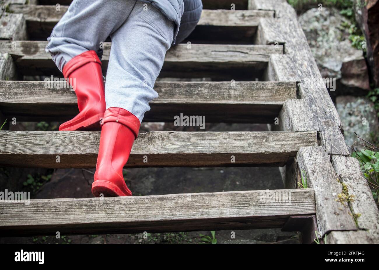 Little boy climbing weathered wooden stairs. Rainy season and children concept. Stock Photo