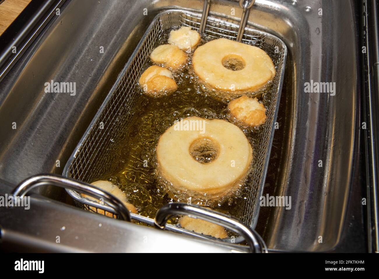 Delicious doughnuts and doughnut holes being cooked in a oil fryer showing the delicious snack frying in oil Stock Photo