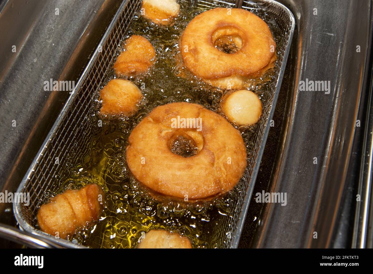 Delicious doughnuts and doughnut holes being cooked in a oil fryer showing the delicious snack frying in oil Stock Photo