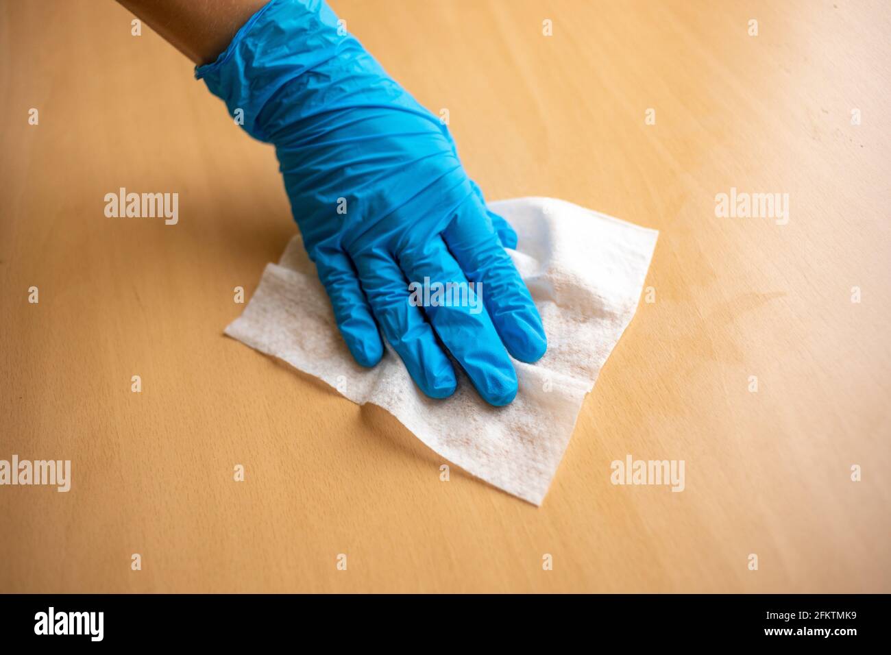 Woman's hand in blue gloves sanitizing cleaning home office wood table