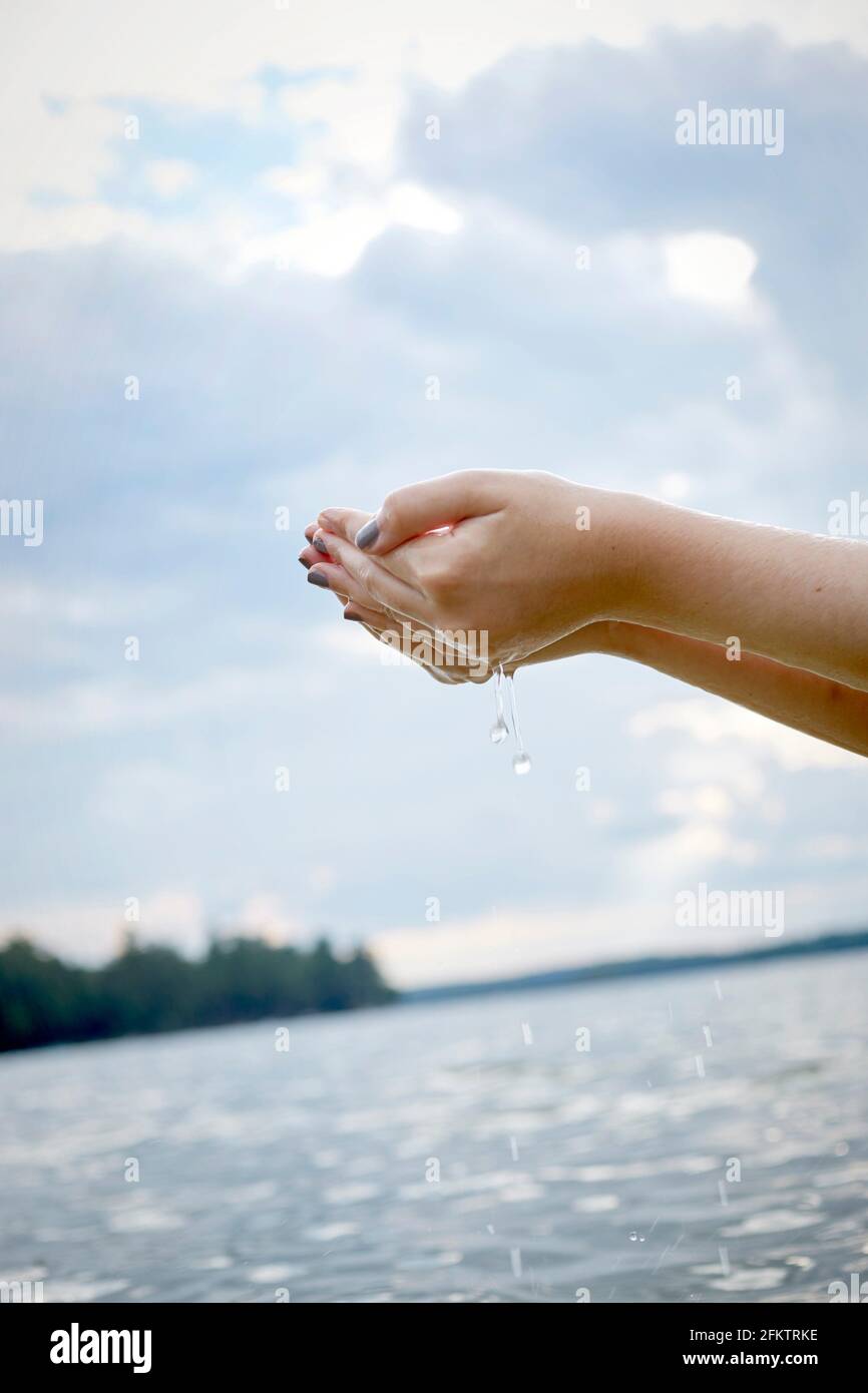 A girls hands holding water while standing in a lake, with nail polish and water dripping. Stock Photo
