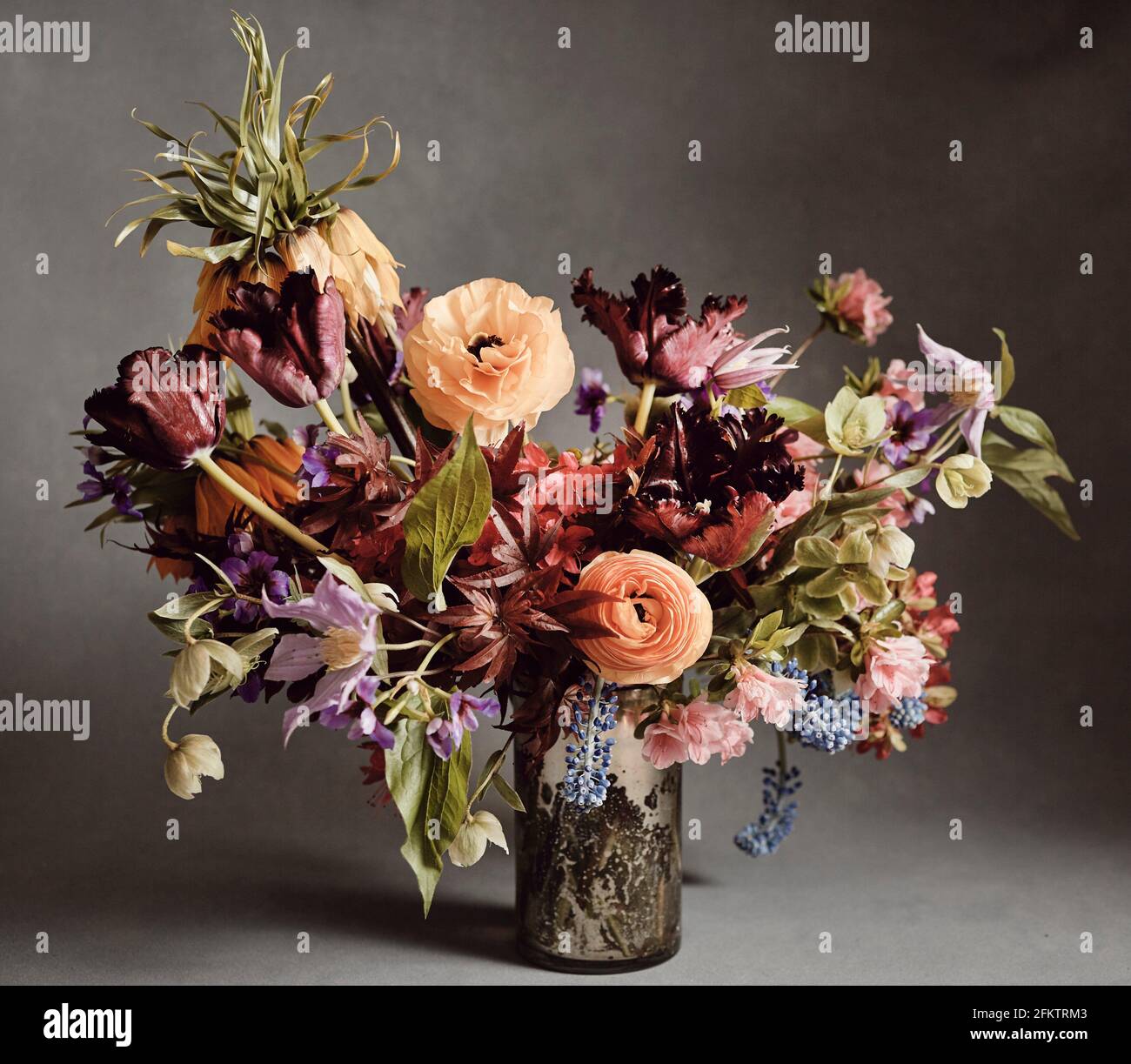 A bouquet of red, orange, purple, green and blue flowers in a mercury glass vase against a grey backdrop. Stock Photo