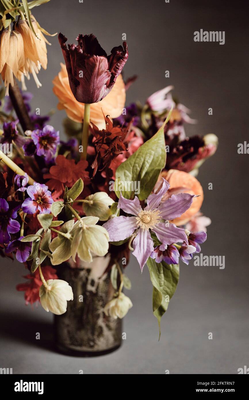 A bouquet of red, orange, purple, green and blue flowers in a mercury glass vase against a grey backdrop. Stock Photo