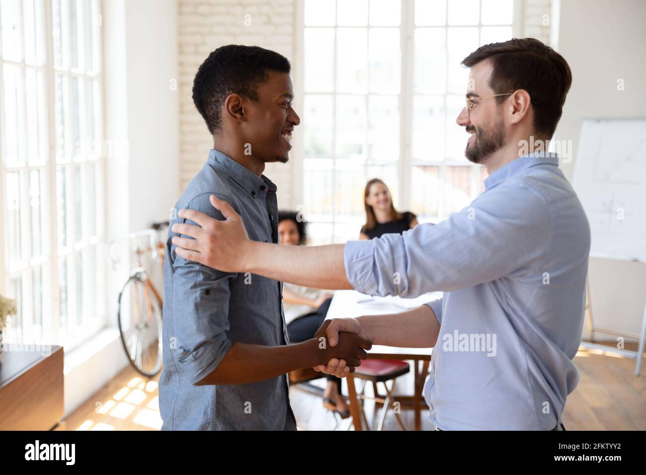 Smiling young male boss shaking hands with african employee. Stock Photo