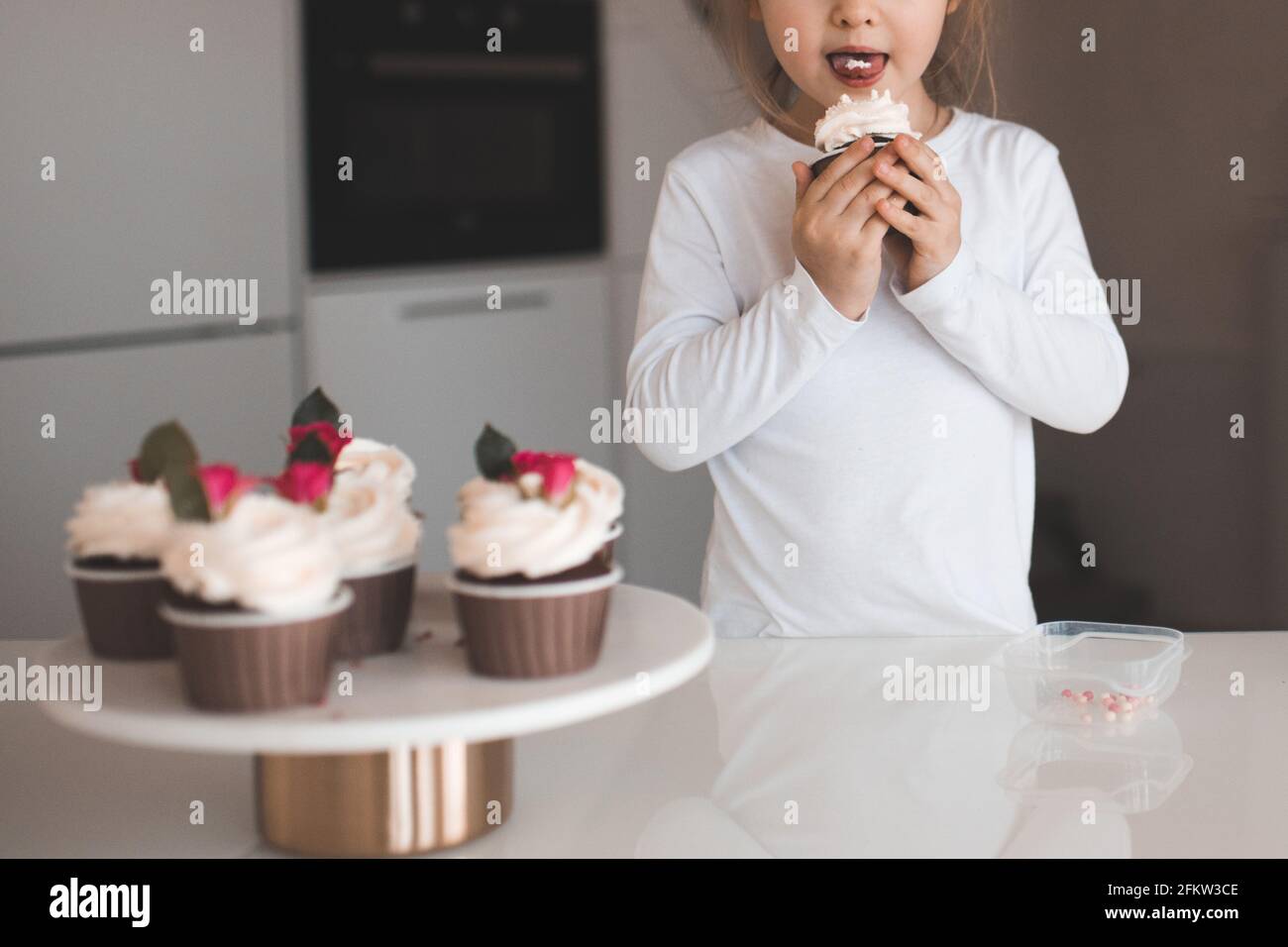 Cute baby girl 23 year old eating tasty cupcakes with cream on top at