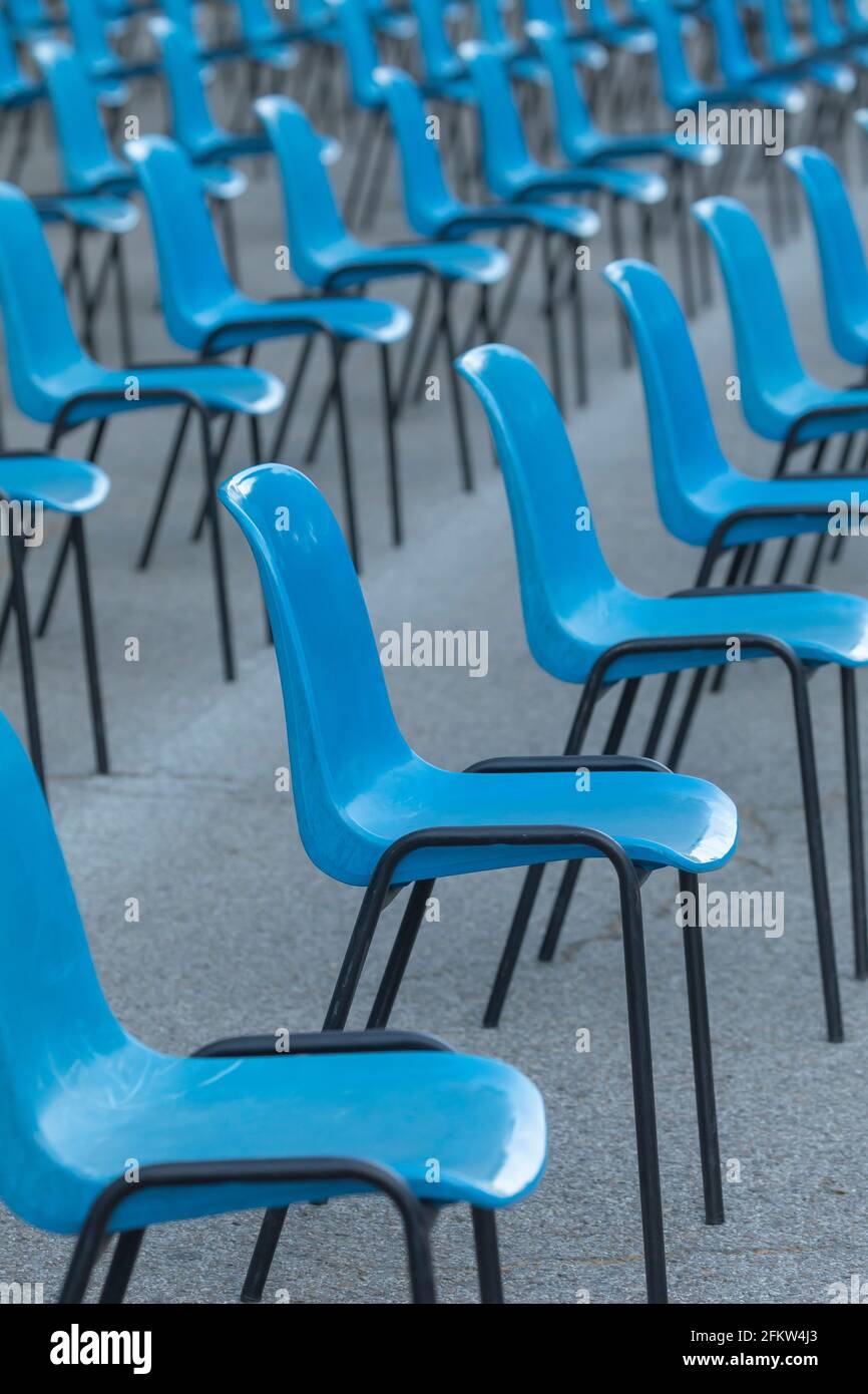 Rows and columns of nondescript blue plastic chairs, consecutive, arranged in a line, at similar