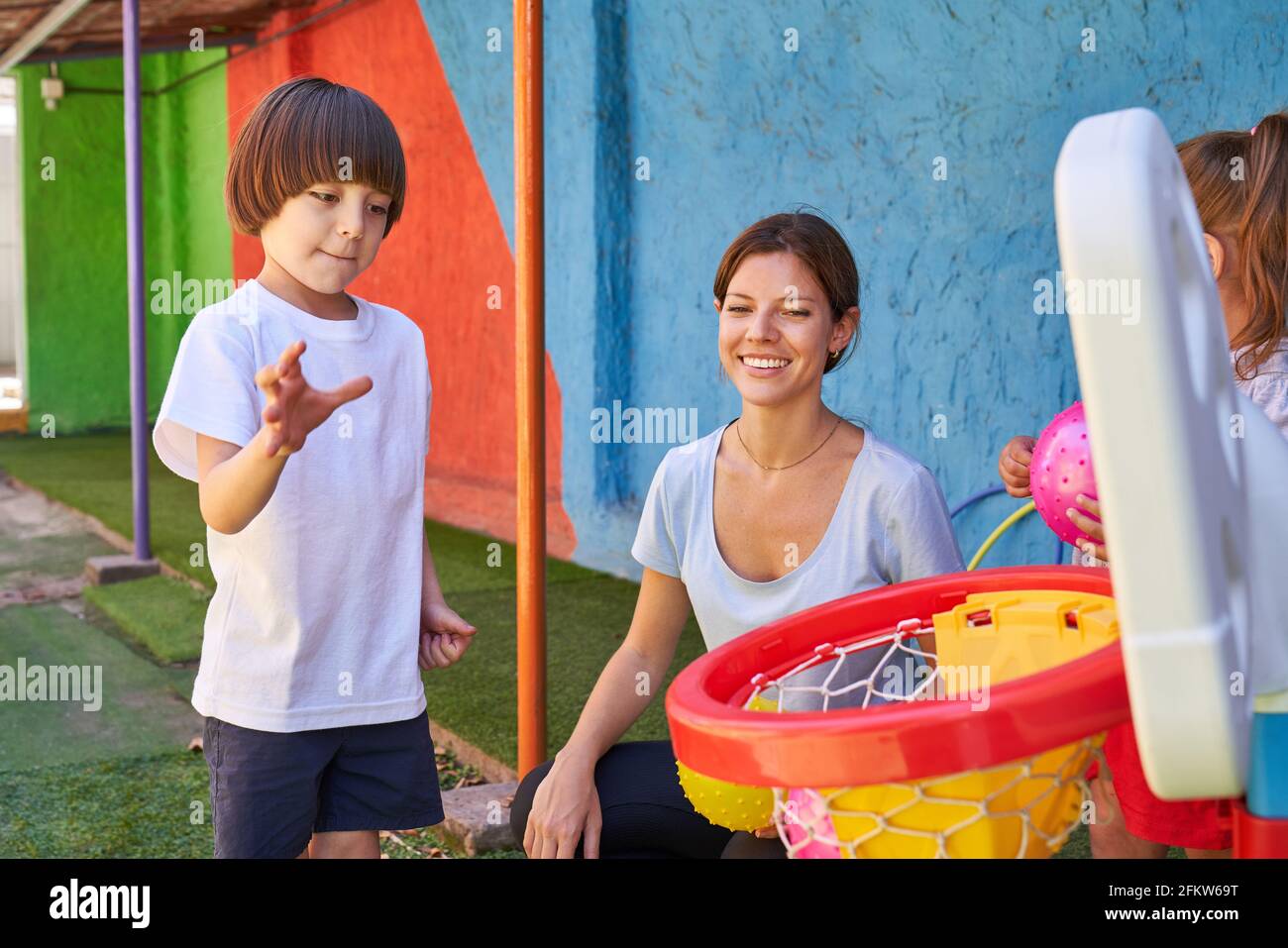 Boy throws a ball into the net during basketball training with gym teacher in kindergarten Stock Photo
