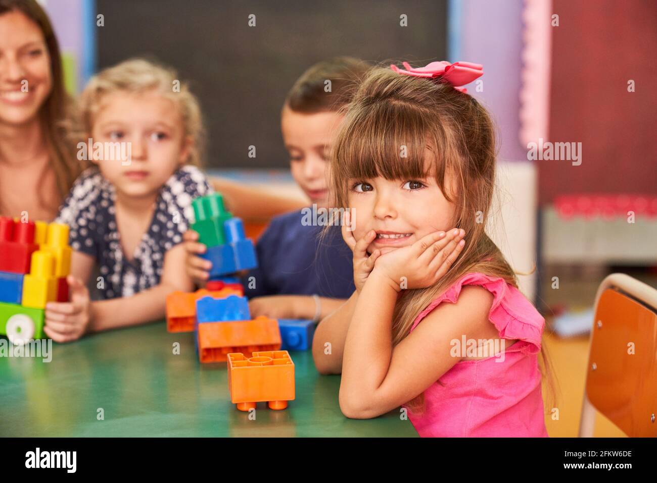 Little girl and her friends in kindergarten or after-school care center play with colorful building blocks Stock Photo