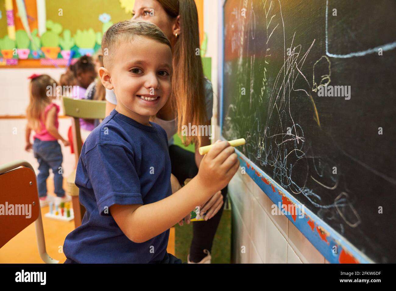 Boy and teacher at the blackboard in preschool while creative painting and drawing Stock Photo