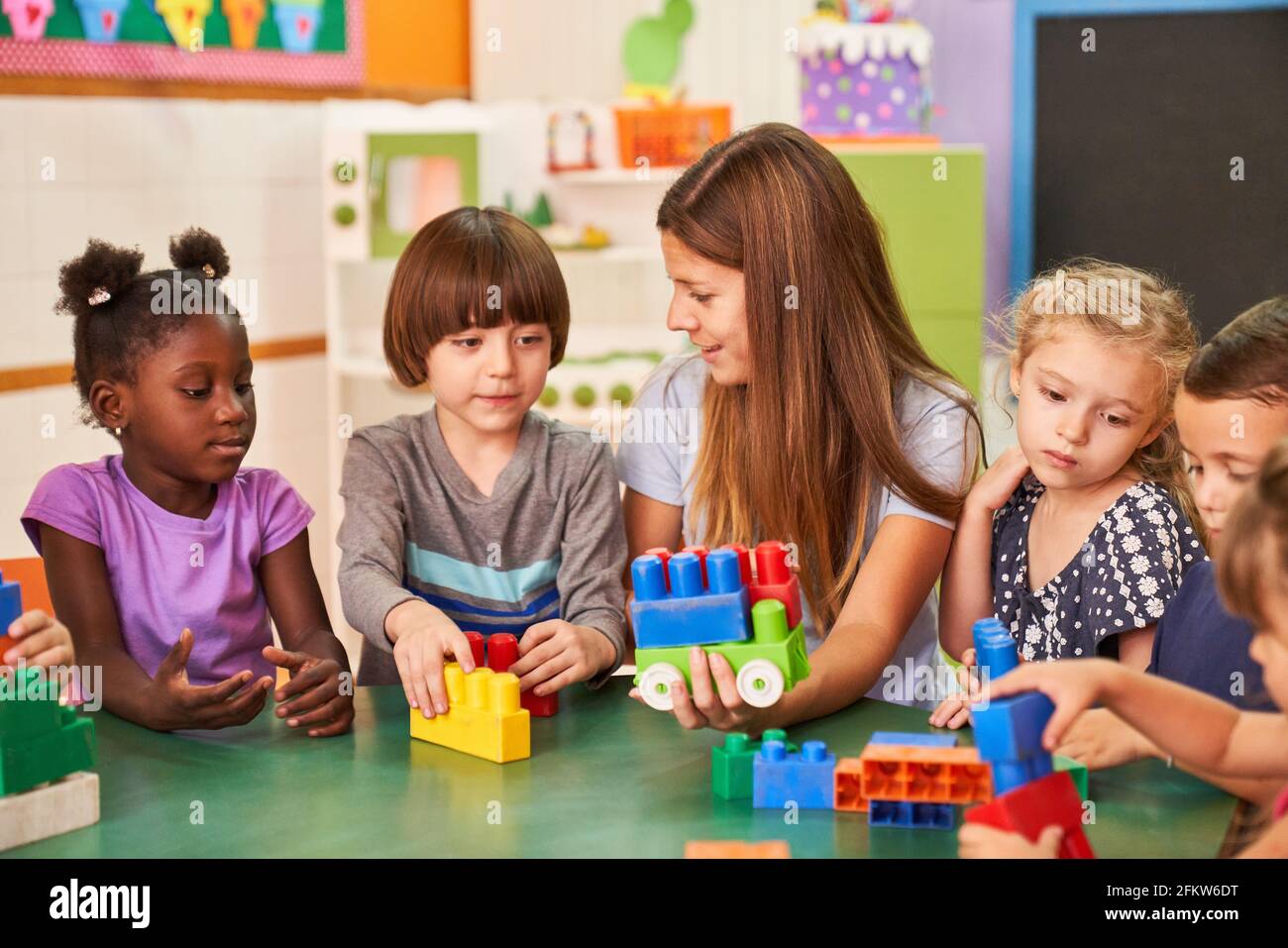 The educator and children in the international kindergarten play together with colorful building blocks Stock Photo