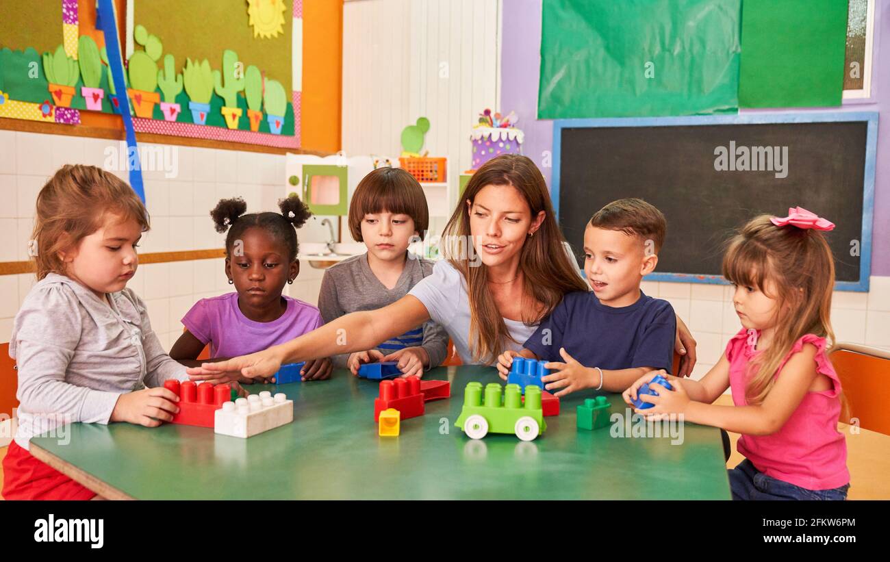 Kindergarten teacher or childminder and children playing with building blocks in kindergarten Stock Photo