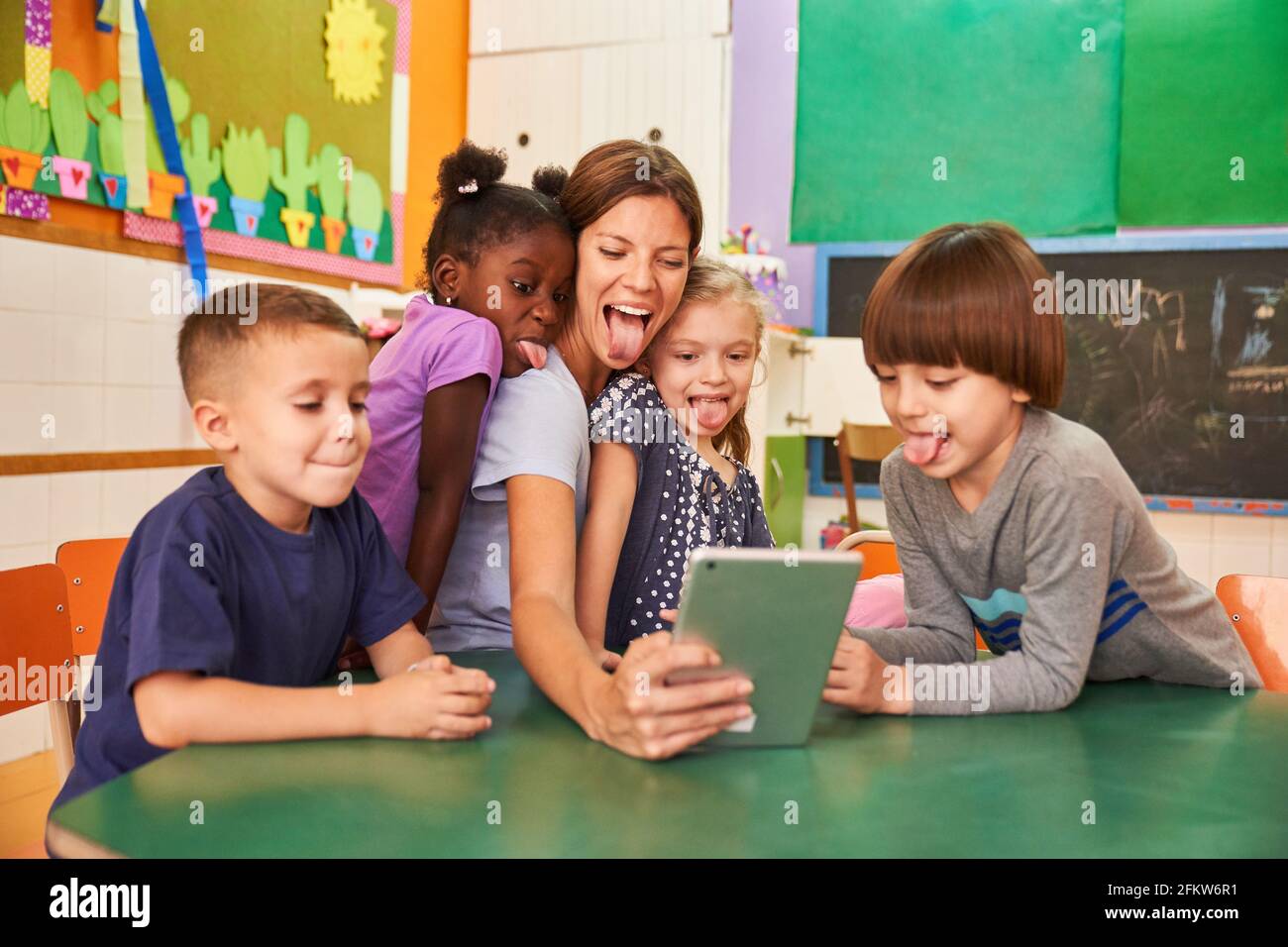 Children and educators cheekily show their tongue for a selfie on the tablet computer online Stock Photo