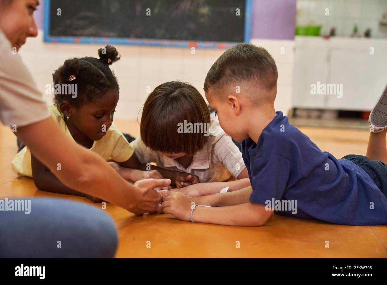 Children play together on the floor in kindergarten or after-school care center with a kindergarten teacher Stock Photo