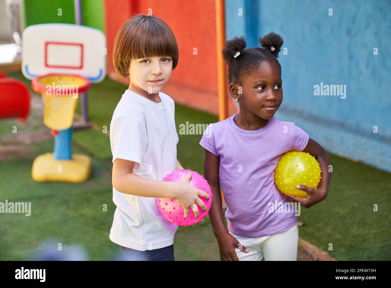 Two children as multicultural friends playing ball in the sports class in kindergarten Stock Photo