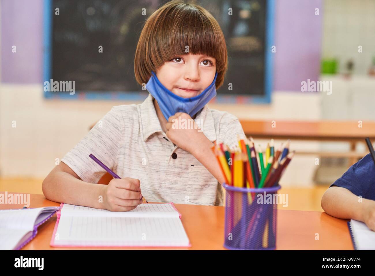 Boy with mask because of Covid-19 and coronavirus in elementary school does homework Stock Photo