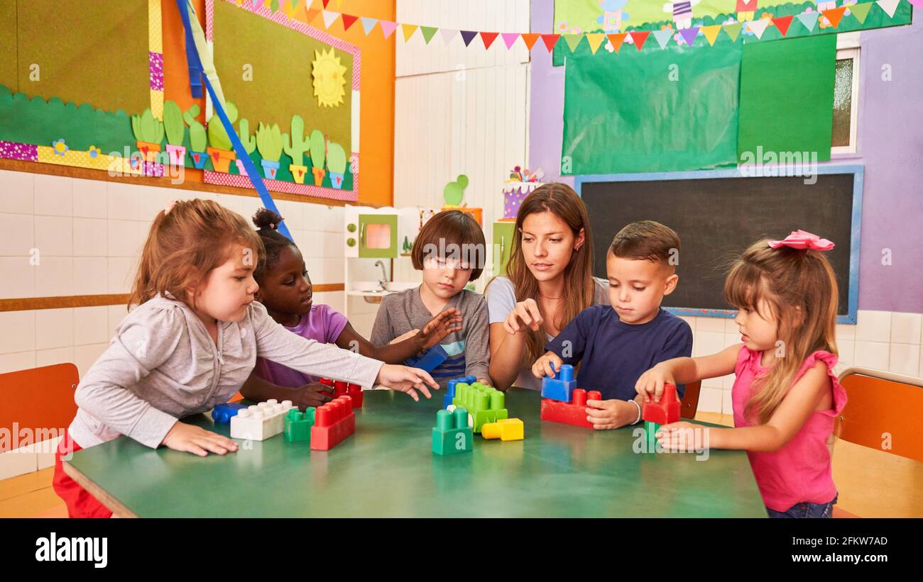 Kindergarten teacher and children play with building blocks together in