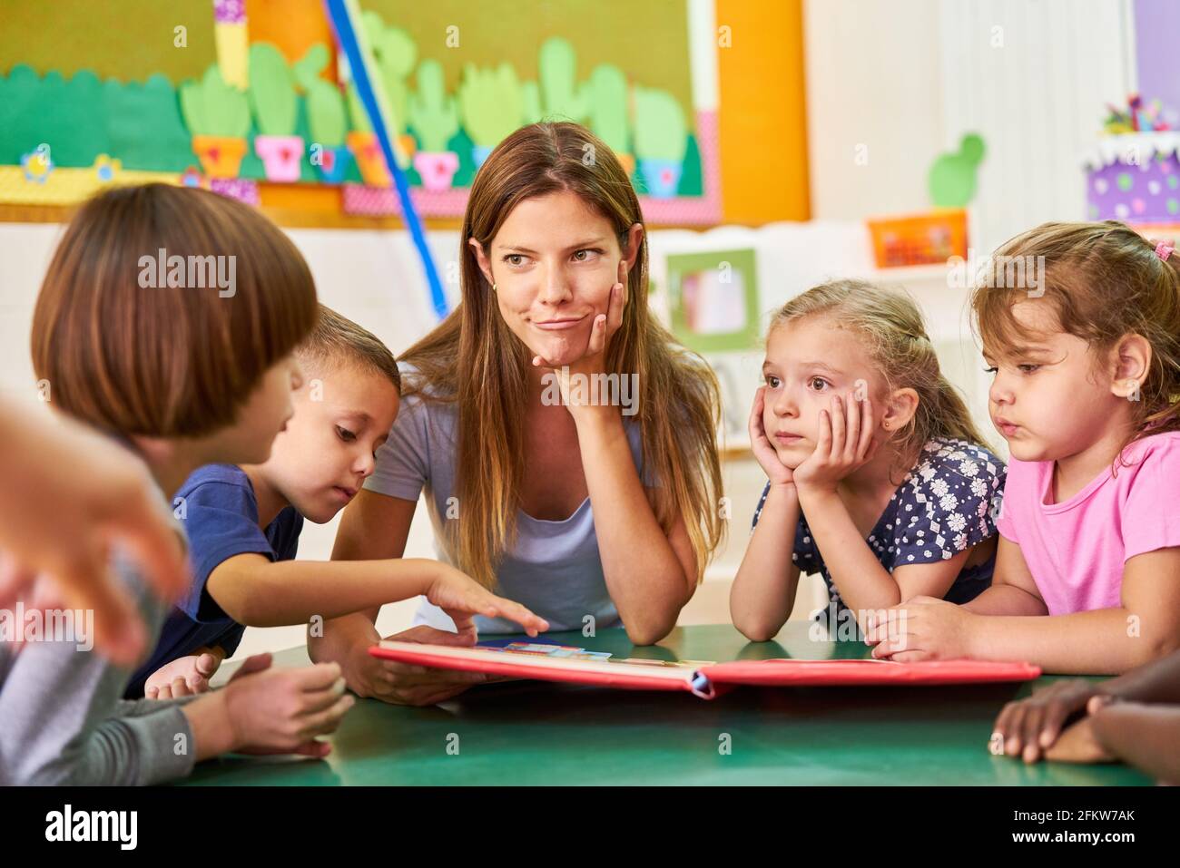 Childminder or kindergarten teacher and children read and play together in kindergarten Stock Photo
