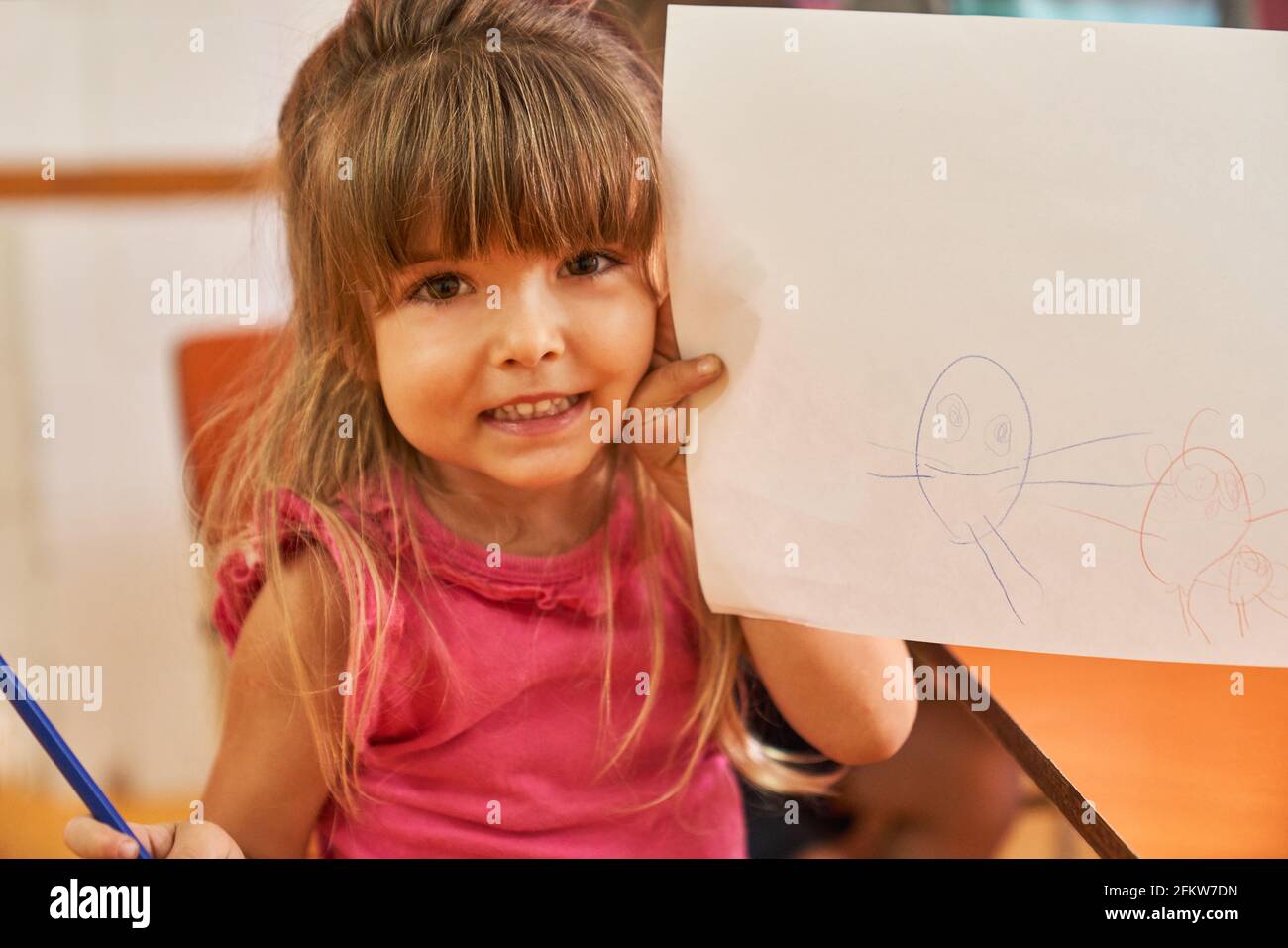 Girl proudly shows a creative drawing on a sheet of paper in