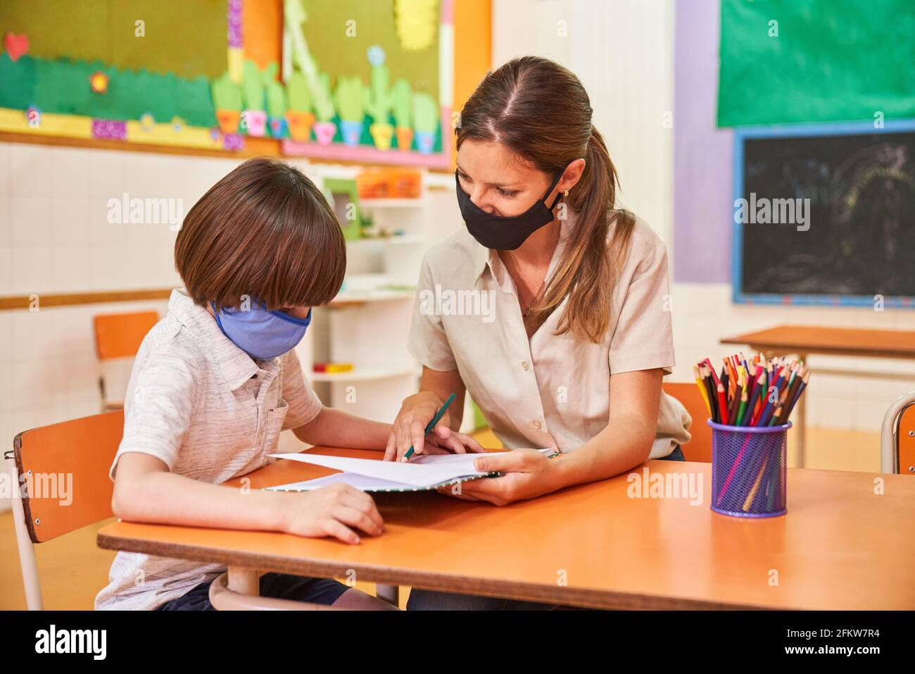 Teacher and child with mask because of Covid-19 do homework together Stock Photo