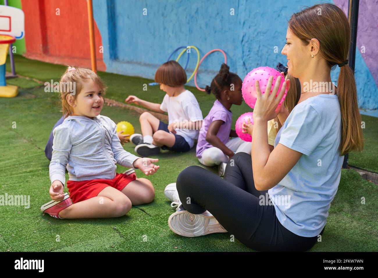 Sports teacher plays ball with children in physical education class outside in front of the day care center or after-school care center Stock Photo