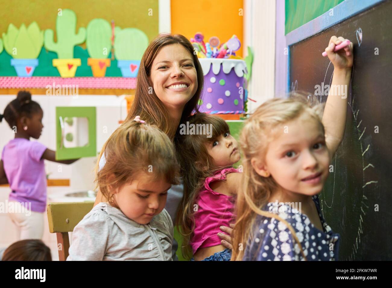 Kindergarten teacher and group of children have fun painting on the school blackboard in kindergarten Stock Photo