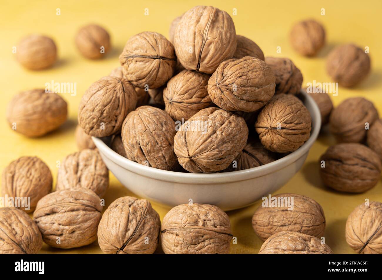 Close-up of a pile of walnuts inside a bowl on a yellow background Stock Photo