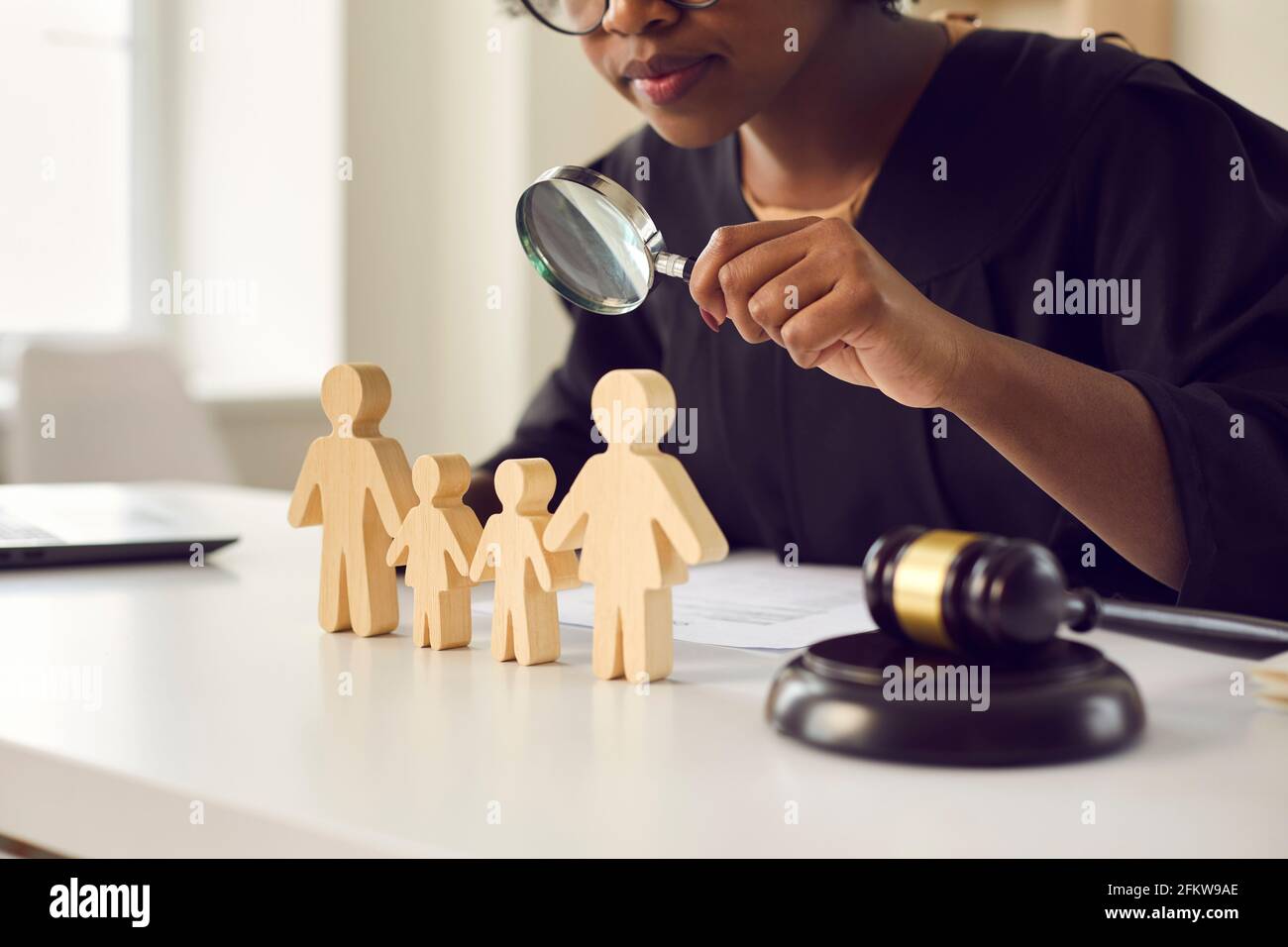 Judge with magnifying glass looking at little family figures standing on her table Stock Photo