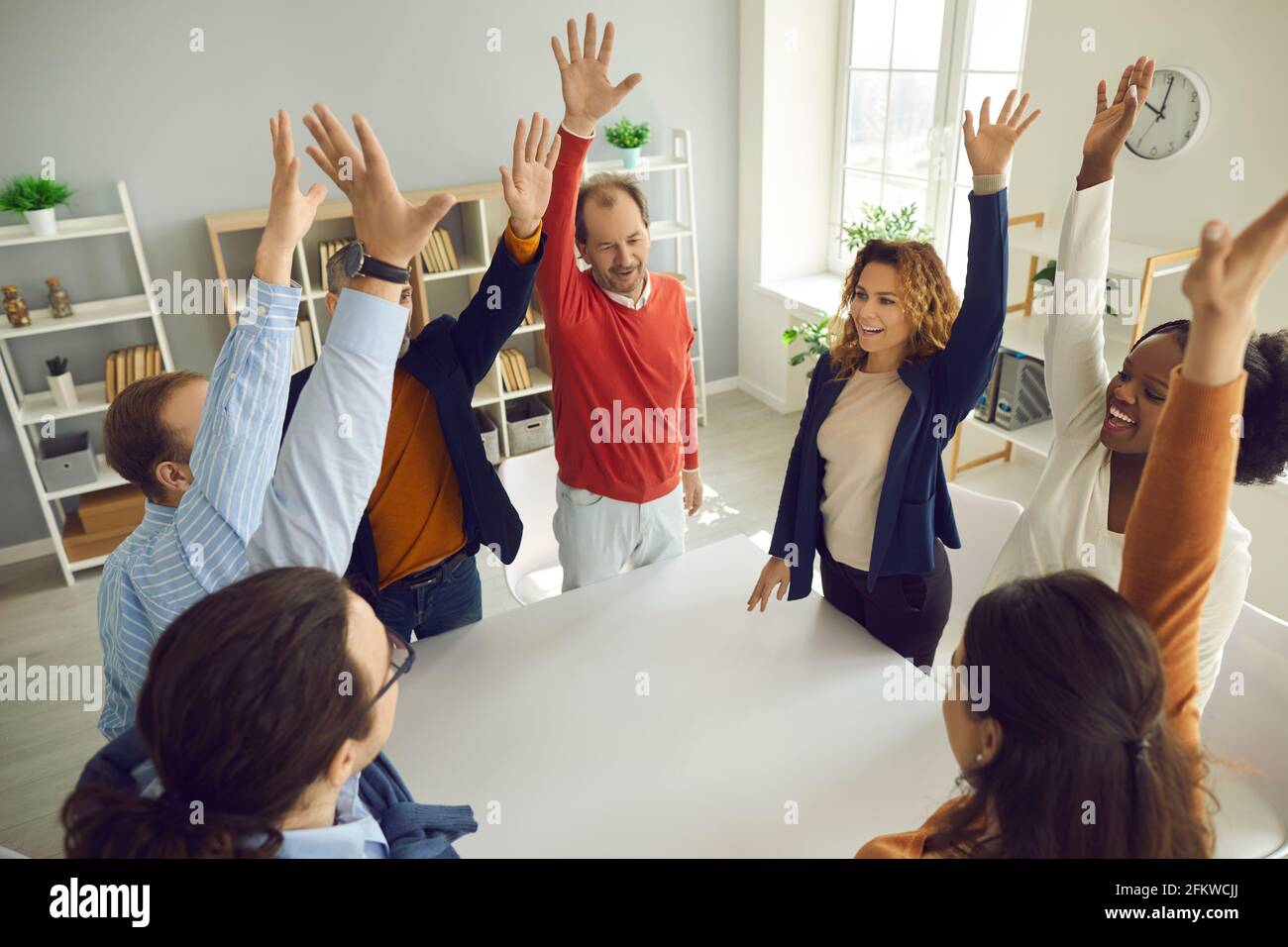 Diverse multiracial different age team standing around table with raised hand Stock Photo