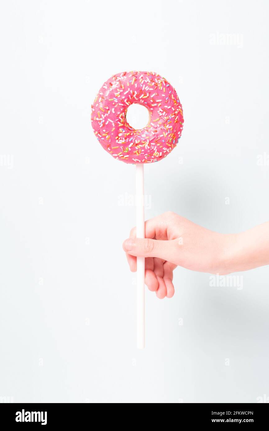Funny yummy pink donut on stick in child's hand like lollipop. Minimalism. Donut day.  Stock Photo