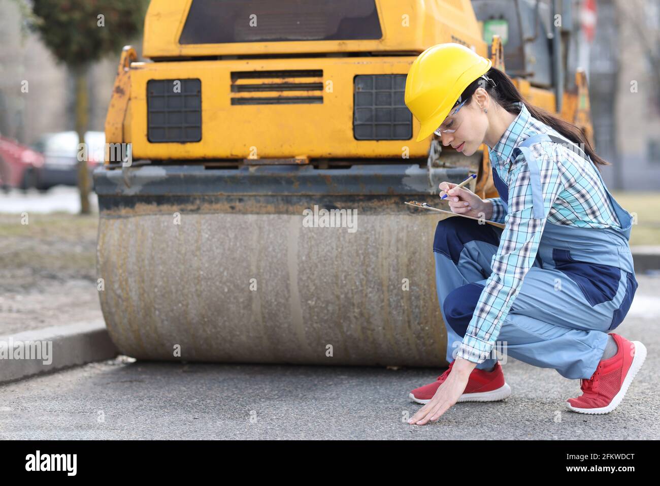 Woman examines asphalt pavement in front of asphalt paver Stock Photo