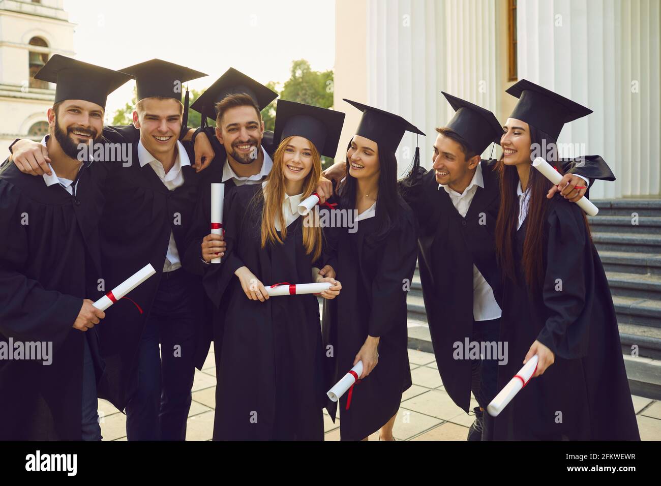 Group of positive students university graduates mates standing, hugging and holding diplomas in hands Stock Photo