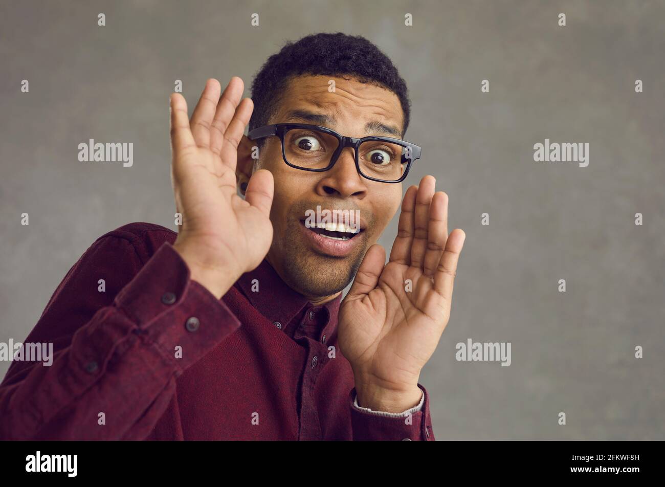 Studio portrait of a scared young black man in glasses looking at the camera and panicking Stock Photo