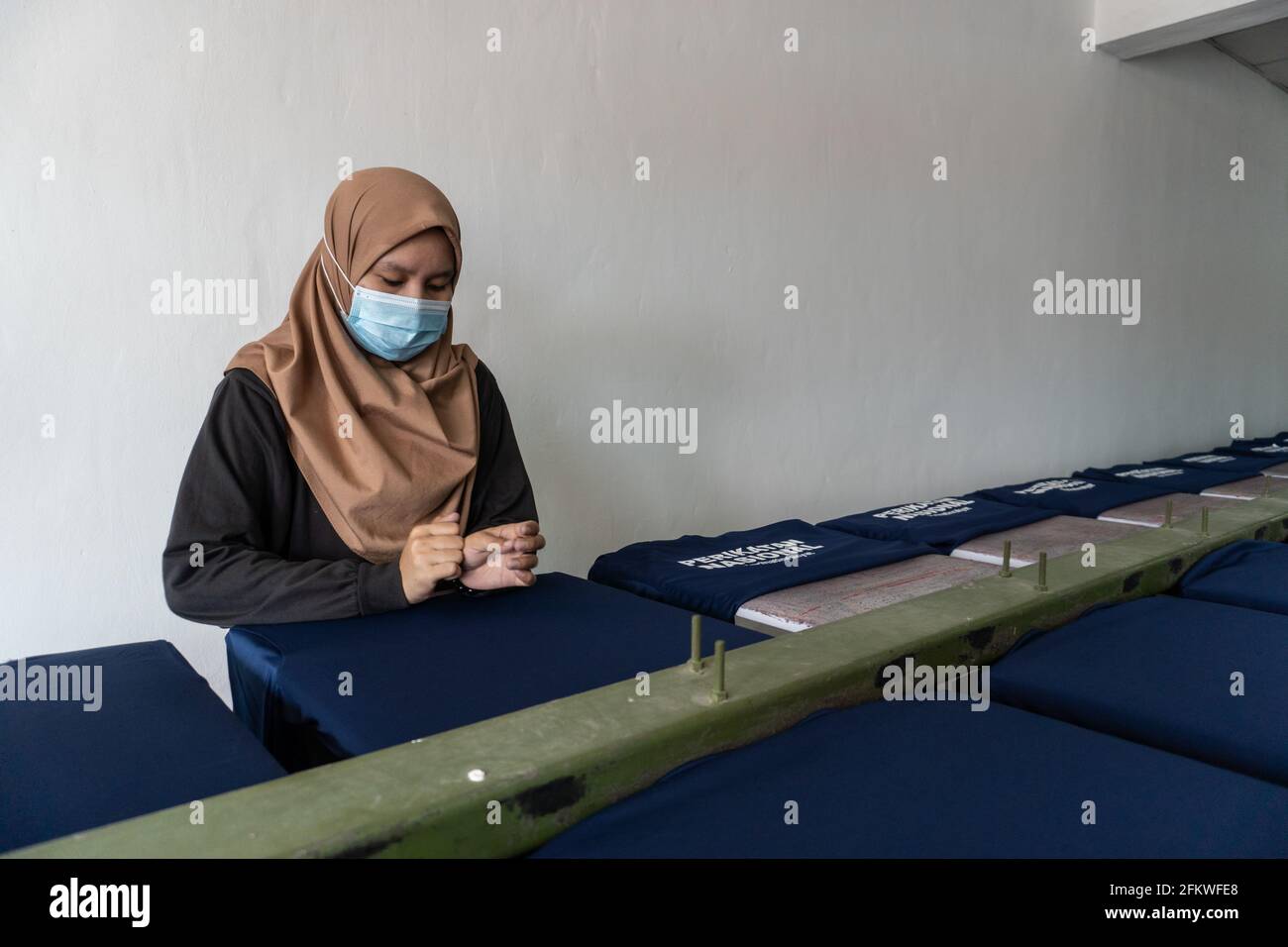 Kota Kinabalu, Sabah, Malaysia-March 05, 2021 : Lady worker with medical face mask preparing t-shirt for printing in the silk screen printing table oa Stock Photo