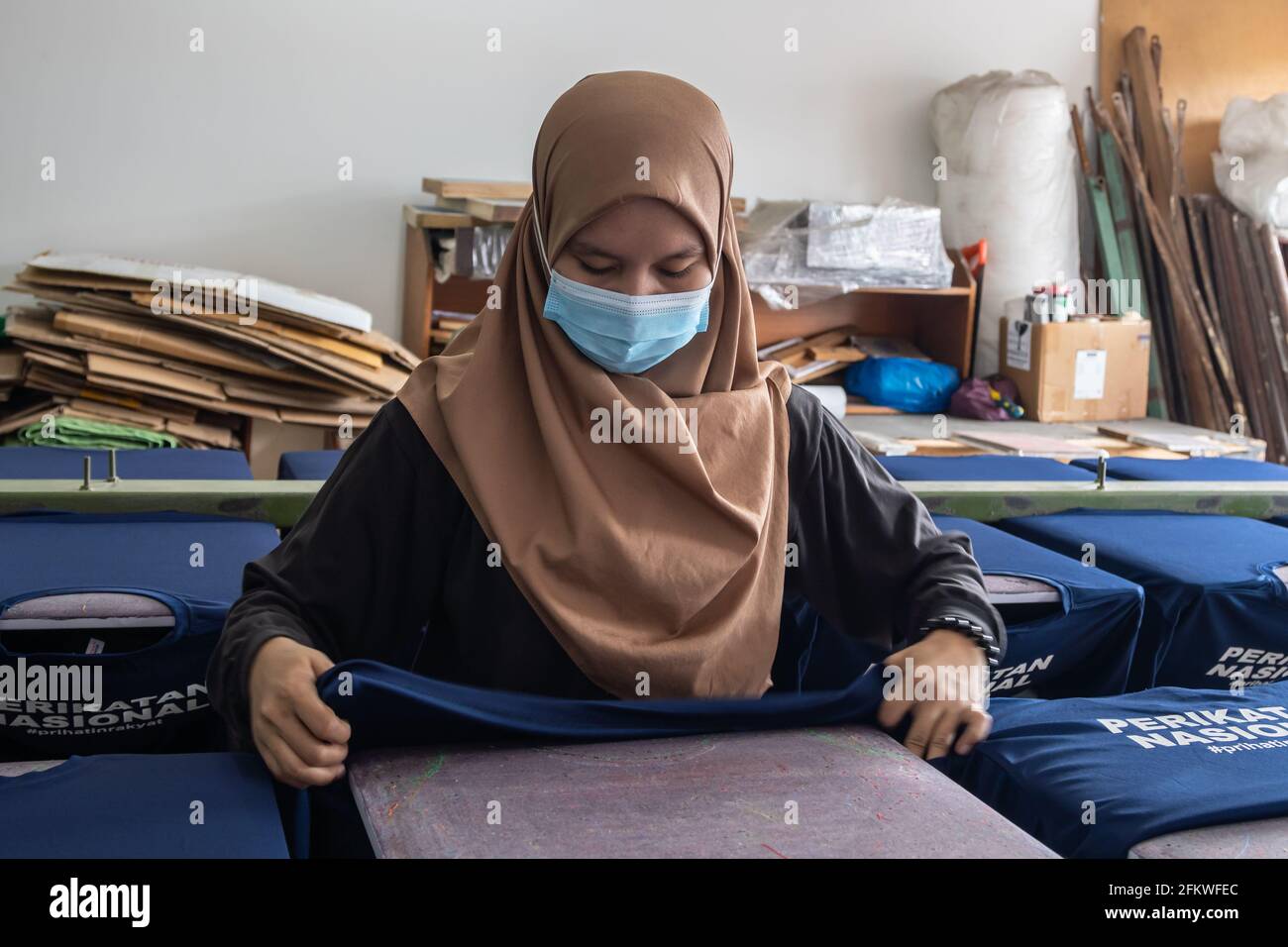 Kota Kinabalu, Sabah, Malaysia-March 05, 2021 : Lady worker with medical face mask preparing t-shirt for printing in the silk screen printing table oa Stock Photo
