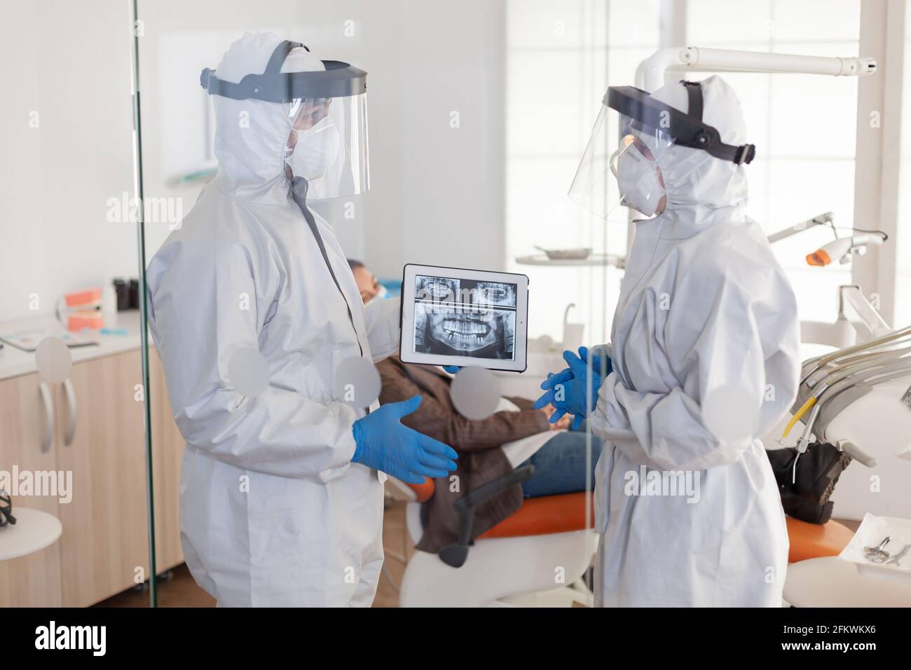 Dentist doctors in overall using tablet explaining dental x ray in stomatologic office during coronavirus. Man wearing face shield and mask showing to nusrse radiography using digital device Stock Photo